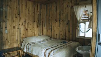 Una habitación de madera con una cama, una mesita y una ventana con cortinas.