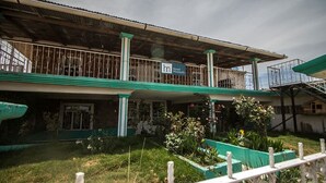 Un edificio de dos pisos con fachada verde y blanca, un balcón con barandilla de metal, y un cartel que indica que es un hotel.