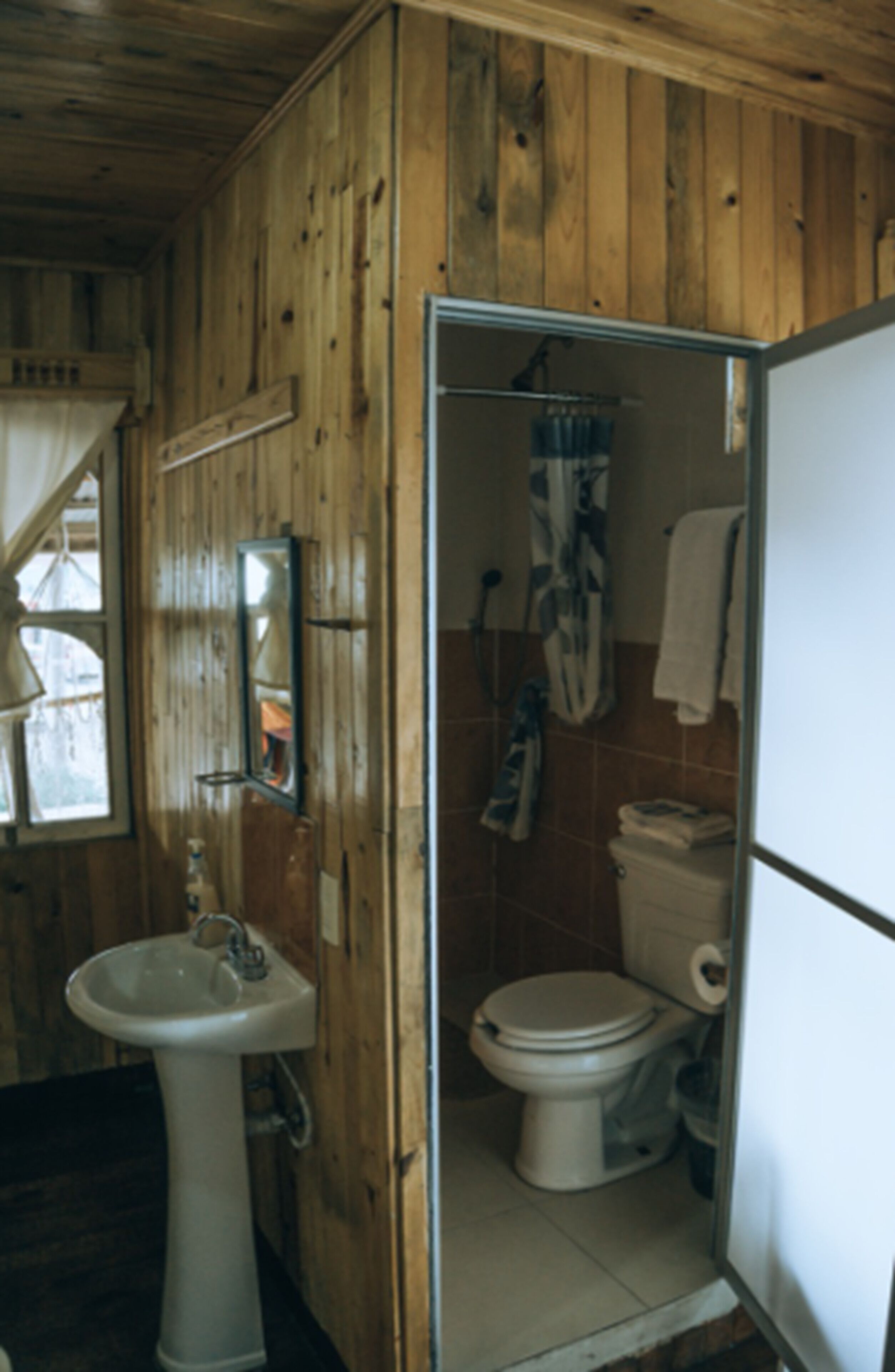 Une salle de bain avec des murs en bois, un lavabo, des toilettes et un espace douche.