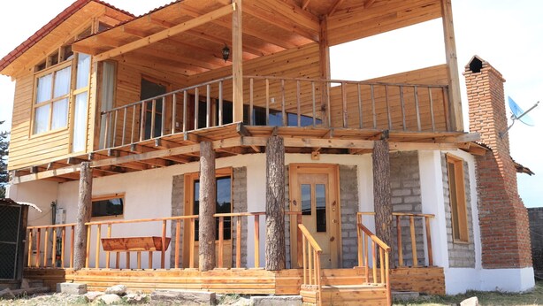 Una casa de madera de dos pisos con balcón, chimenea y antena parabólica.