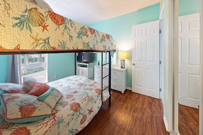 Une chambre avec un lit superposé, une télévision, une petite commode blanche et une porte.