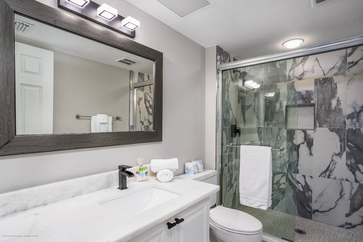 A bathroom with a large mirror, a sink, a toilet, and a glass-enclosed shower area.