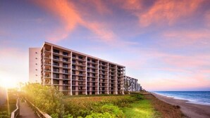 Un hotel de varios pisos con balcones, situado cerca de una playa bajo un cielo despejado.