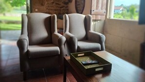 A room with two armchairs, a small table with a tray, a stone wall, a window with a view of greenery, and a wall-mounted light fixture. - Rural house (pet-friendly) where you will only listen to nature. (Rianxo, A Coruña)