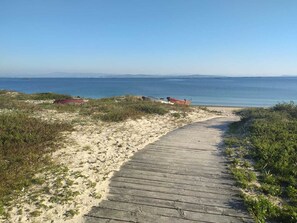 Une plage de sable avec une promenade en bois menant à l’eau, un bateau rouge et une petite construction rouge.