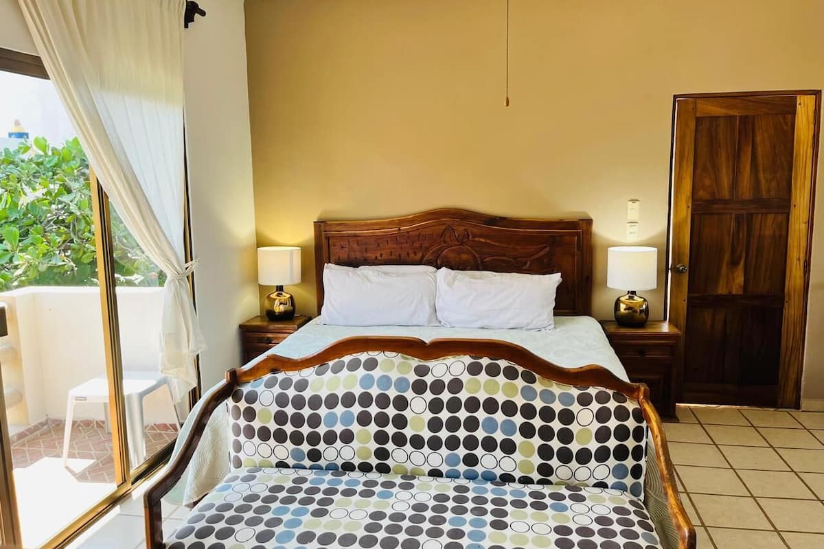 Un dormitorio con cama, dos mesitas de noche, una silla, una puerta de madera y vistas a zonas verdes.