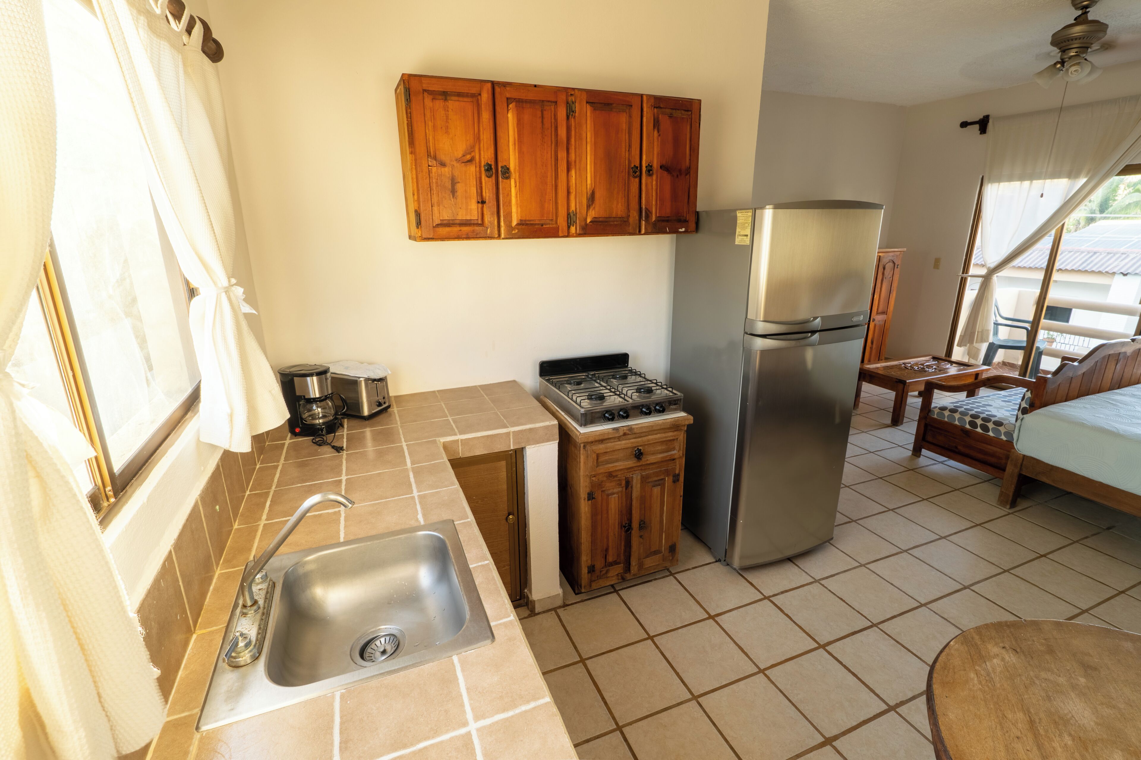 A compact kitchen with a sink, stove, and refrigerator, wooden cabinets, and a small dining area with a chair and table.
