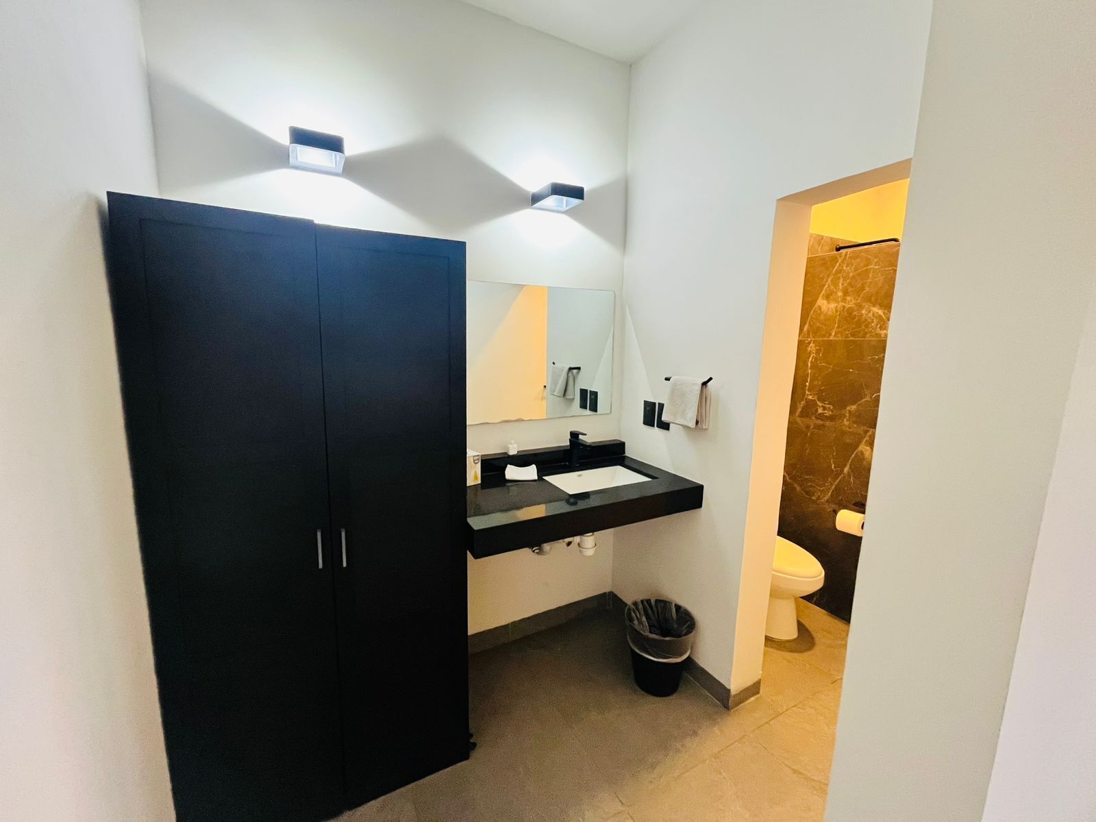A modern bathroom with a black wardrobe, a sink, a mirror, and a toilet.