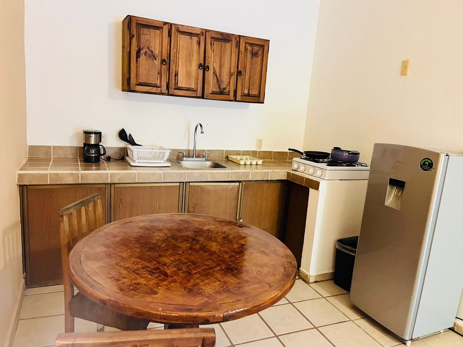 A kitchen with wooden cabinets, a sink, a stove, a refrigerator, and a round wooden table.