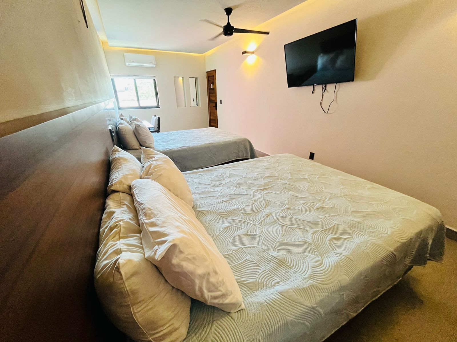 A bedroom with a bed, pillows, a ceiling fan, a TV, and a window.