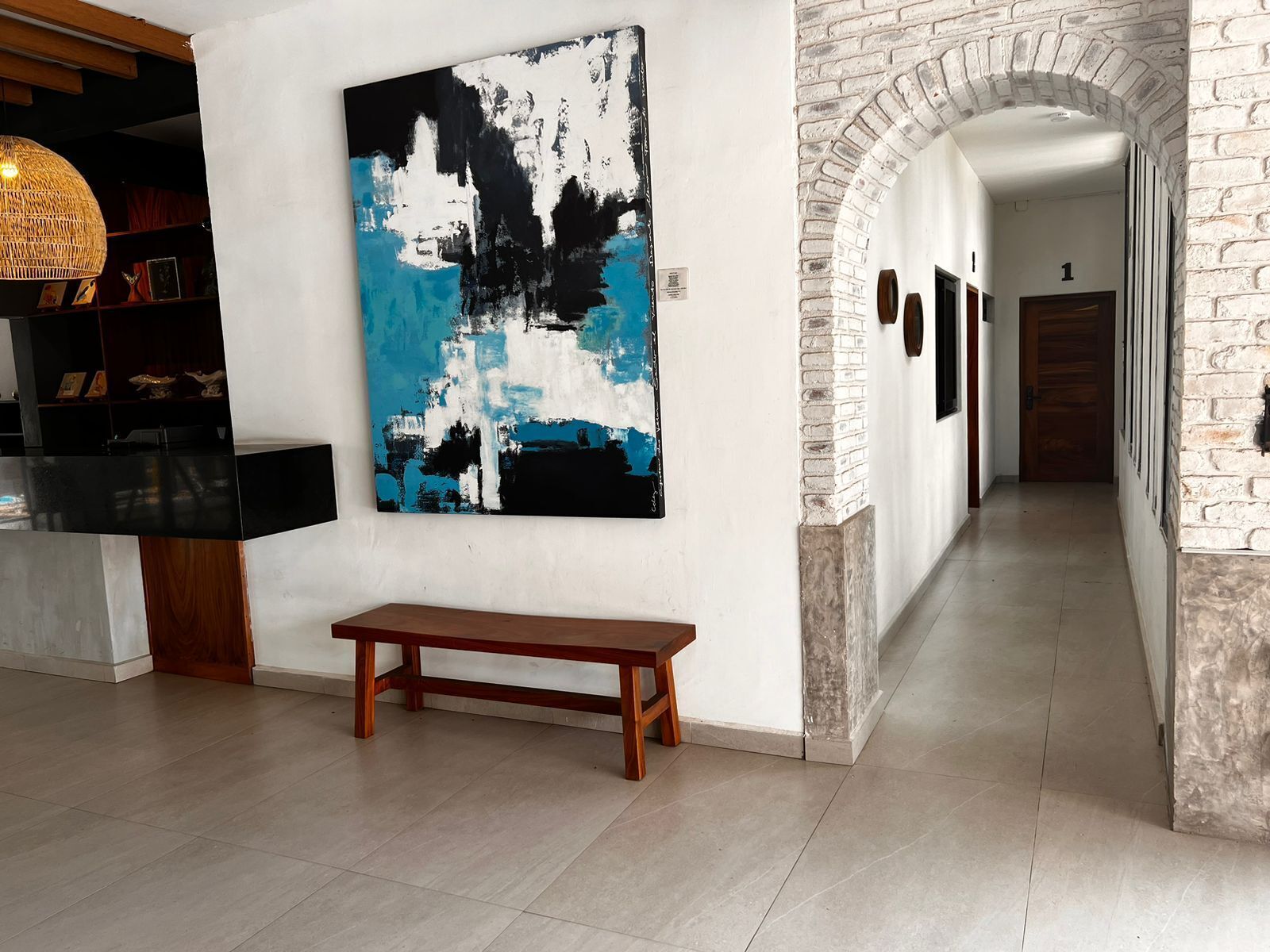 A hallway with a large abstract painting, a wooden bench, and a brick archway.