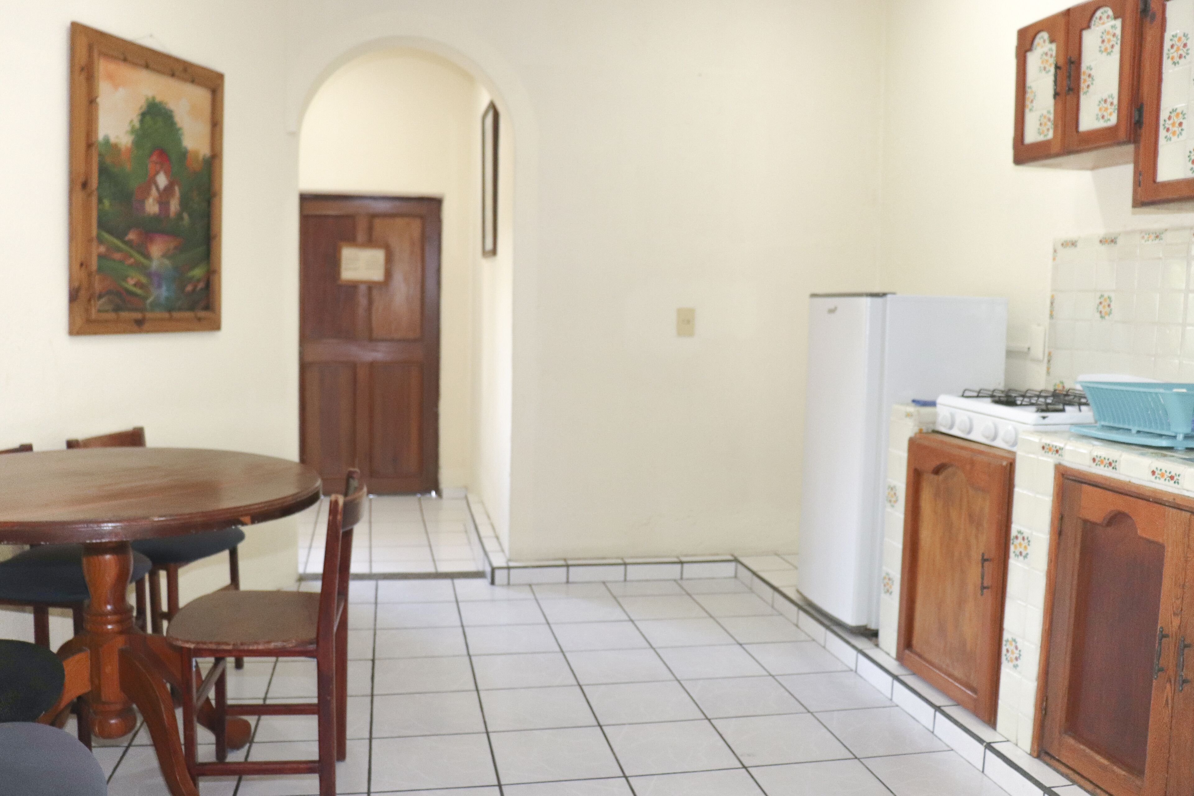 A dining area with a wooden table and chairs, a kitchen with a stove and cabinets, and a door leading to another room.