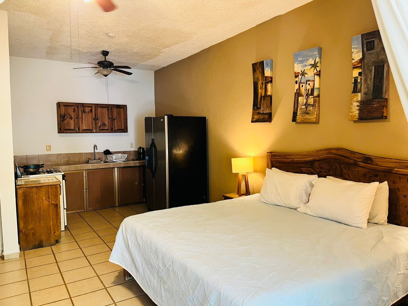 A hotel room with a bed, a refrigerator, a sink, and a ceiling fan.