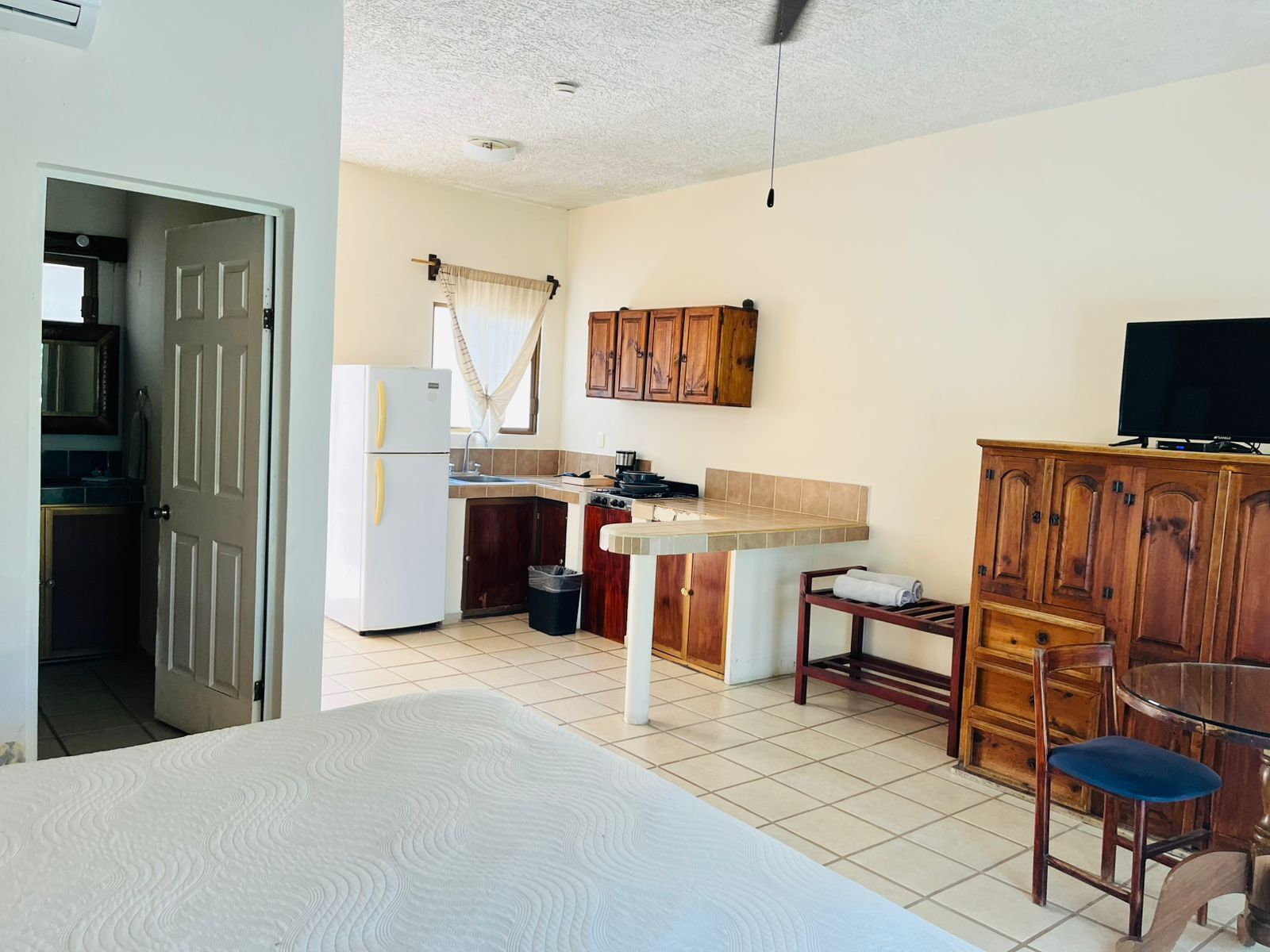 A compact hotel room with a bed, a kitchenette, a TV, and a small dining area.
