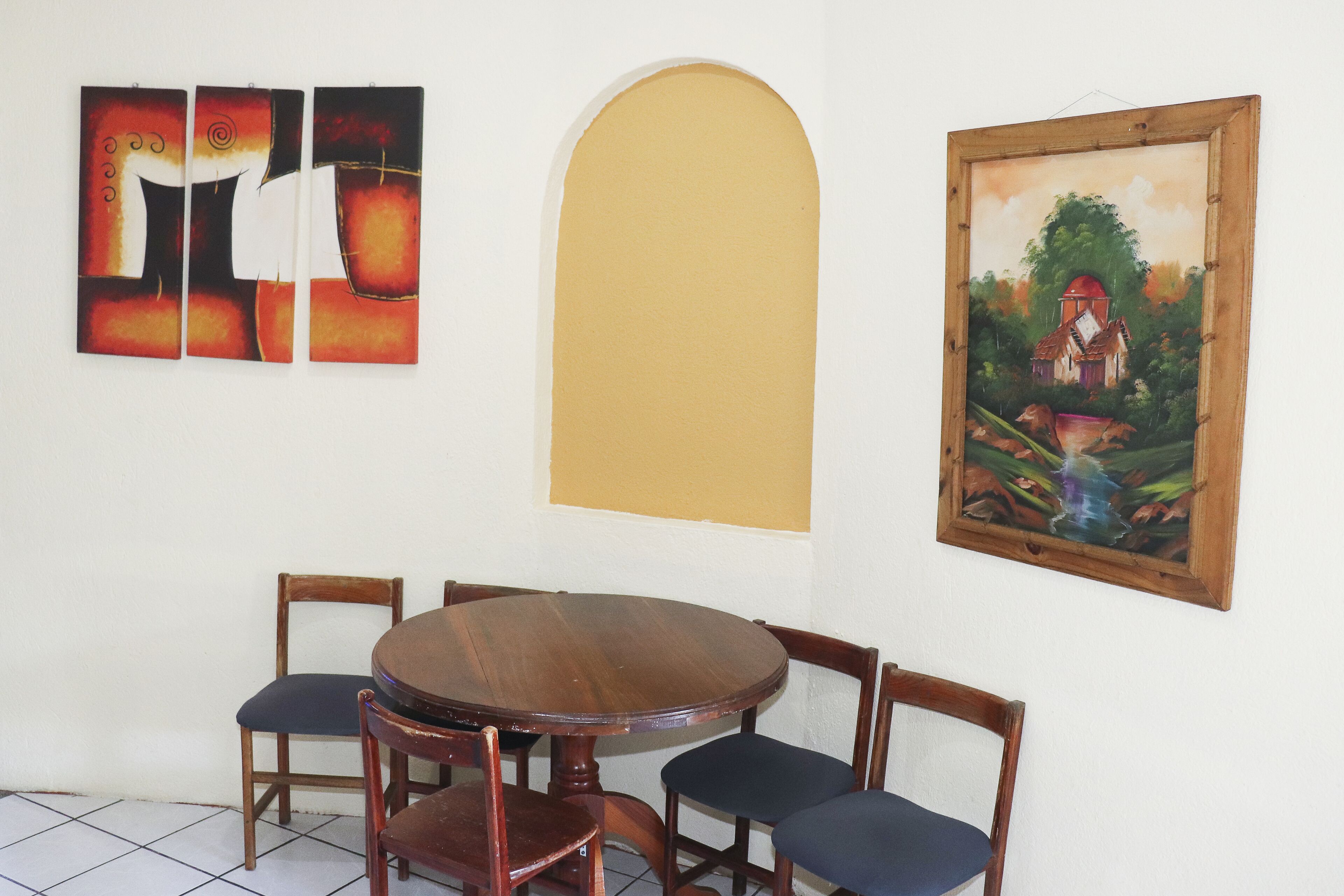 Un comedor con una mesa redonda de madera y cuatro sillas, una pared con tres obras de arte, y un piso de baldosas.