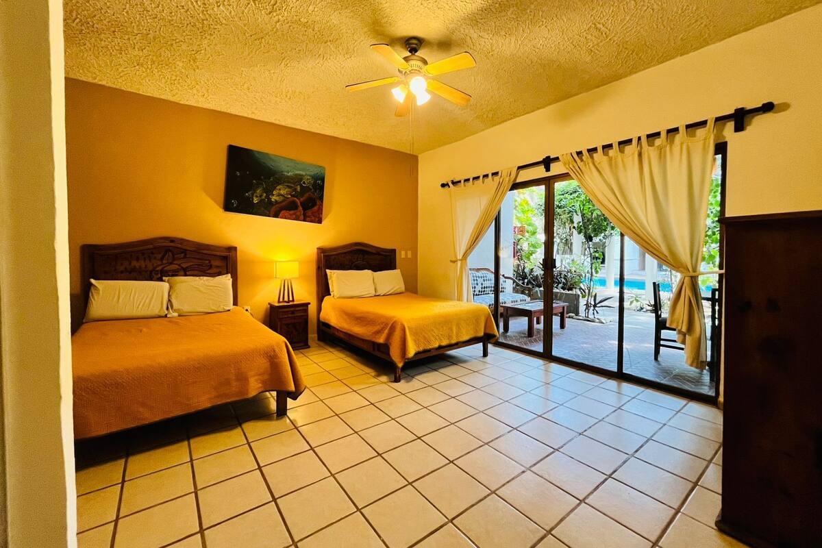 Una habitación de hotel con dos camas, un ventilador de techo, un cuadro y vistas al exterior.