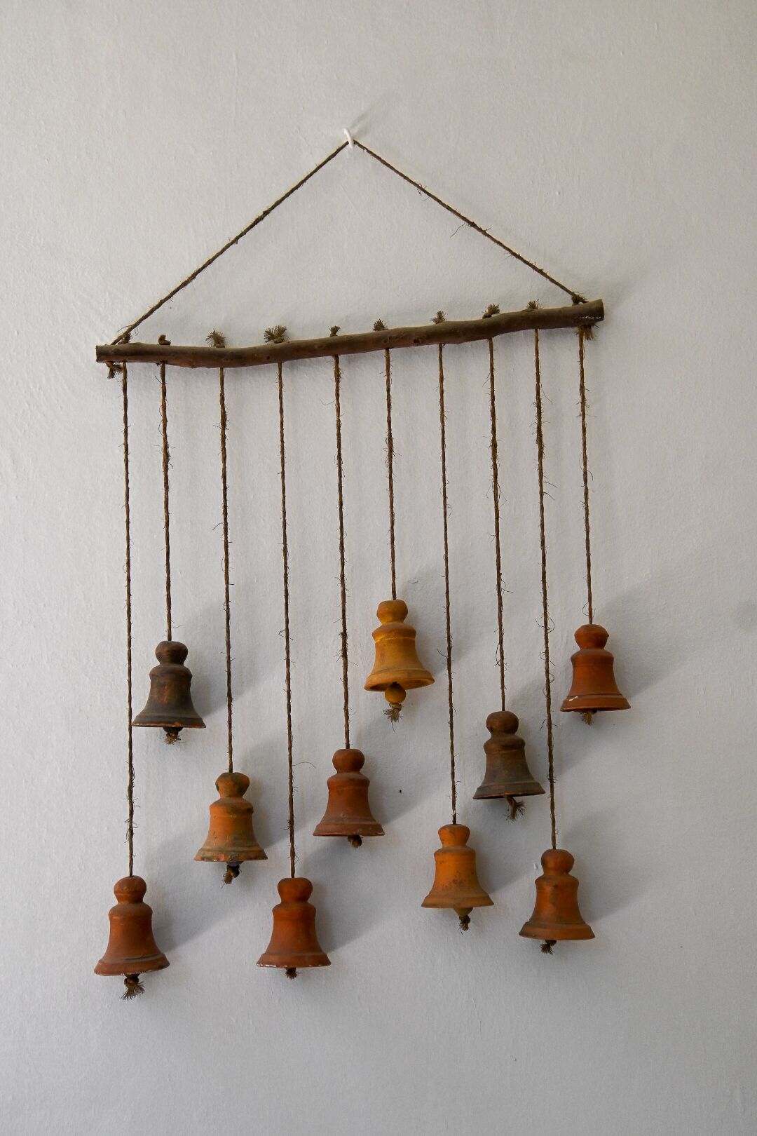 A wall-mounted wind chime with multiple bells hanging from a horizontal branch.
