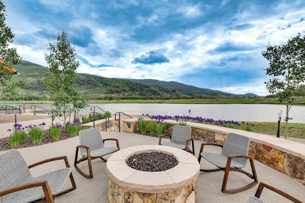 Un patio con mobiliario exterior y una chimenea, con vistas a un lago y colinas.