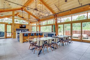 Un comedor interior amplio con una larga mesa y sillas, vigas de madera en el techo y ventanas grandes que ofrecen vistas al exterior.