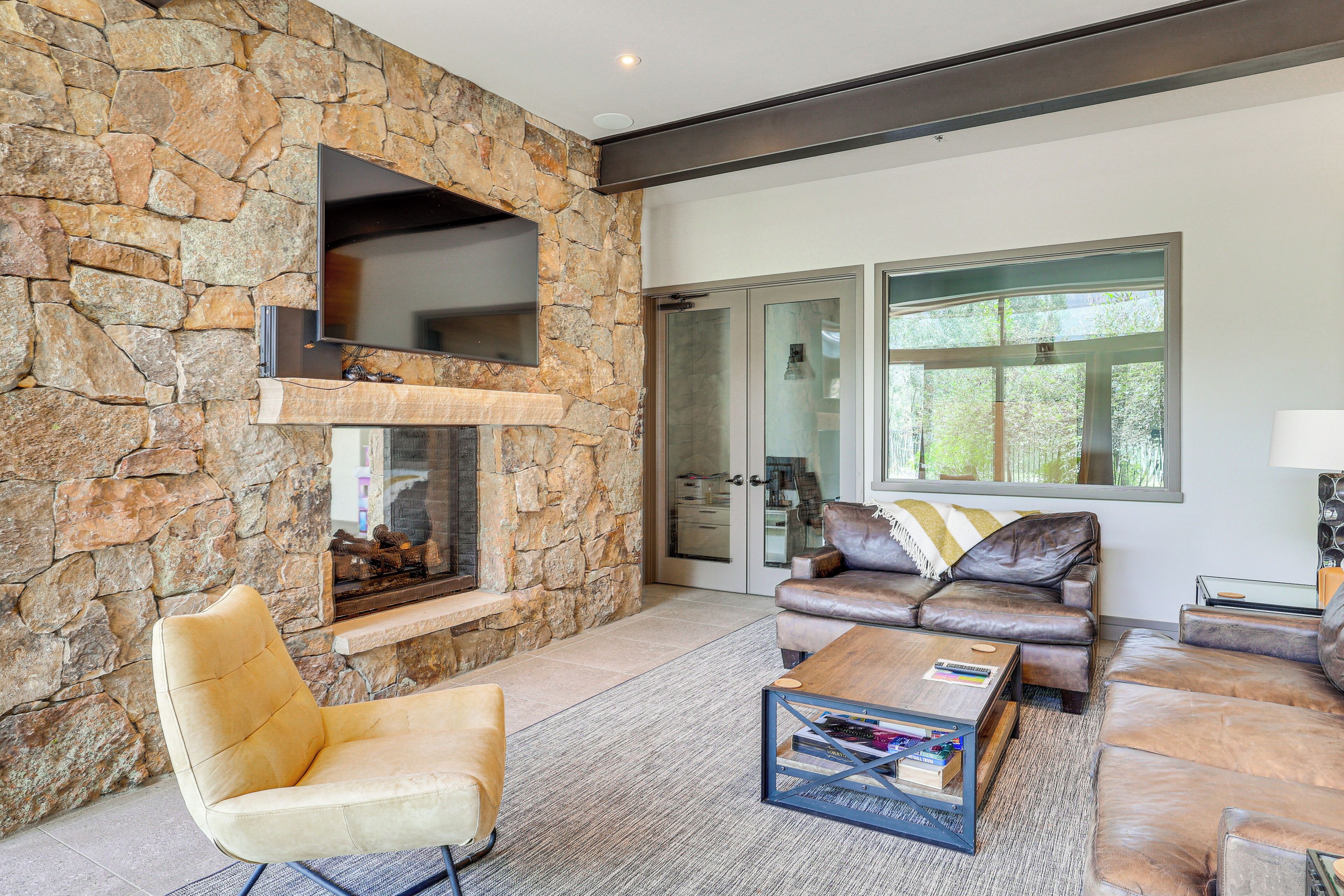 A modern living room with a stone wall, leather furniture, a fireplace, and large windows.