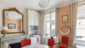 A dining area with a round table, red chairs, a white tablecloth, a large mirror, and a kitchen in the background.