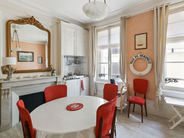 Un comedor con una mesa redonda, sillas rojas, un mantel blanco, un espejo grande y una cocina al fondo.