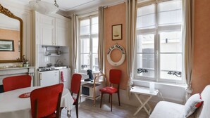 A compact kitchen with white cabinets, a stove, and a dining area with red chairs.