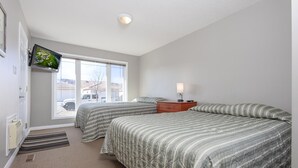 Ein Schlafzimmer mit zwei Betten, einem an der Wand montierten Fernseher, einem Fenster mit Blick ins Freie und einem Nachttisch mit Lampe.