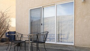Ein Außenbereich mit Tisch und Stühlen, eine Schiebetür und ein Gebäude mit strukturierter Fassade.