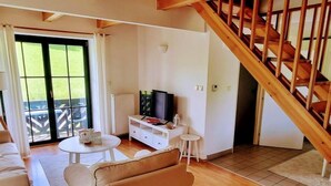 Un salon avec un canapé, une table basse, un téléviseur posé sur un meuble et un escalier.