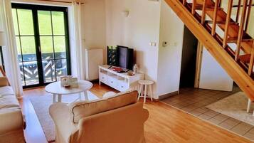 Un salon avec un canapé, une table basse, un téléviseur posé sur un meuble et un escalier.
