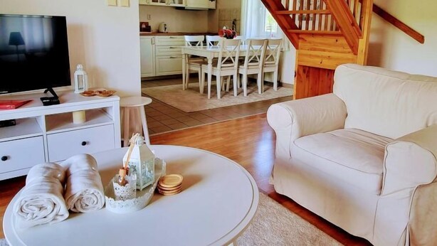 Un salon équipé d’un téléviseur, d’un canapé blanc, d’un coin repas avec une table et des chaises, et d’un escalier en bois.
