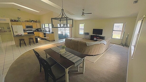 A spacious living area with a dining table, sofa, and a kitchen in the background. - Cozy Oasis (Port St. Lucie)