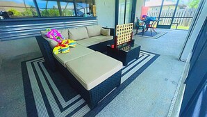 A modern outdoor seating area with a cushioned bench, a coffee table, and a board game. - Cozy Oasis (Port St. Lucie)