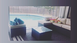 A poolside area with a sofa, a small table, and towels. - Cozy Oasis (Port St. Lucie)