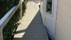 A wooden deck leading to a house with a white exterior and a large window.