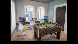 A game room with a foosball table, two computer monitors, and office chairs.