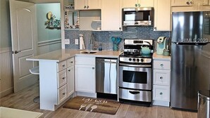 A modern kitchen with white cabinets, stainless steel appliances, and a blue backsplash.