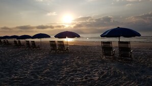 A beach with rows of sun loungers and umbrellas, a calm sea, and a setting sun.