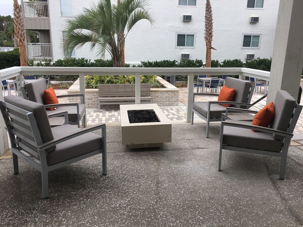 A balcony with outdoor seating, a fire pit, and a view of palm trees and buildings. - Ocean view - Beautiful Penthouse Condo - Large heated pools & Hot Tubs! (Hilton Head Island)