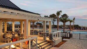 An outdoor dining area with tables and chairs, a pool, and palm trees.