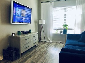 Relax in a cozy living room with a flat-screen TV, comfortable sofa, and natural light pouring in through the window.