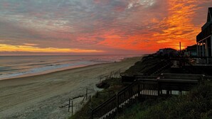 Une plage au coucher du soleil, un escalier en bois et un bâtiment doté d’un toit en pente.
