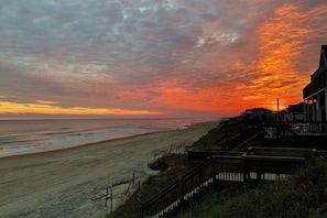 A beach with a sunset, a wooden staircase, and a building with a sloped roof. - Upscale Oceanfront, with Panoramic Views (Emerald Isle)