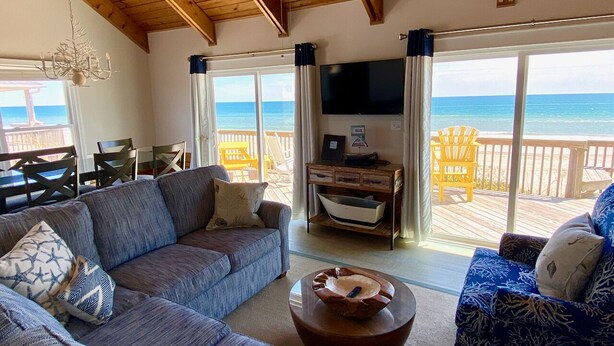 Un salon confortable avec un grand canapé, une table basse et un téléviseur. Il y a un balcon avec vue sur l’océan.