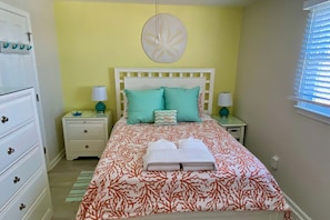 A bedroom with a bed, two bedside tables, a nightstand, a dresser, and a window with blinds.