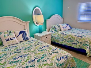 A bedroom with two beds, each with a white headboard, a blue vase on a nightstand, and a mirror above the bed.