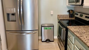 Un réfrigérateur en acier inoxydable, une poubelle, un four à micro-ondes et une cuisinière dans une cuisine.