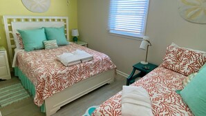 Une chambre à coucher comprenant un lit, des tables de chevet, une fenêtre avec des stores et un mur orné d’un motif circulaire.