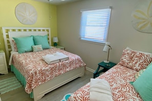 A bedroom with a bed, bedside tables, a window with blinds, and a wall with a circular decoration. - Upscale Oceanfront, with Panoramic Views (Emerald Isle)